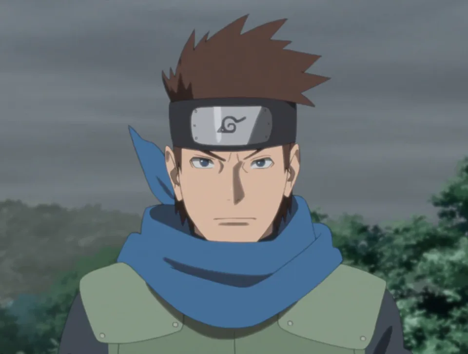 Portrait of a young man with shaggy brown hair, a long blue scarf and a flak jacket, grinning with a confident squint